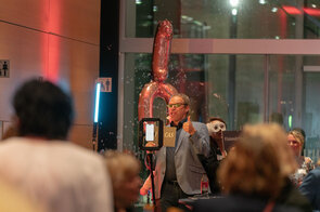 Ein Mann in einem blauen Anzug zeigt Daumen hoch, w&auml;hrend Seifenblasen um ihn herum schweben und eine festliche Atmosph&auml;re schaffen.