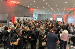 Eine lebhafte Versammlung von Menschen in einem modernen Raum, die angeregt miteinander sprechen und Getr&auml;nke halten.