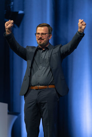 Ein begeisterter Redner auf der B&uuml;hne mit erhobenen H&auml;nden