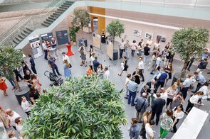 Eine lebhafte Versammlung von Menschen in einem modernen Raum, umgeben von Pflanzen und Informationsst&auml;nden.