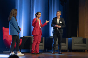 Drei Redner auf der B&uuml;hne w&auml;hrend einer Konferenz