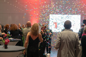 Eine festliche Atmosph&auml;re mit buntem Konfetti, das &uuml;ber eine Gruppe von Menschen in eleganter Kleidung regnet.