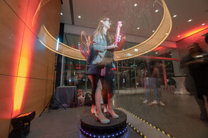 Eine Frau steht in einem beleuchteten Raum und h&auml;lt eine pinke Wasserpistole, w&auml;hrend sie von bunten Lichtern umgeben ist.