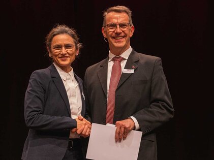 Zwei Personen schütteln sich die Hände auf einer Bühne