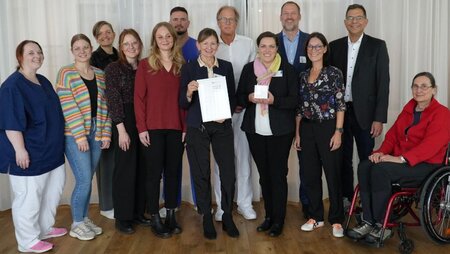 Eine Gruppe von Menschen steht zusammen und lächelt, während sie Urkunden und Auszeichnungen in den Händen halten.