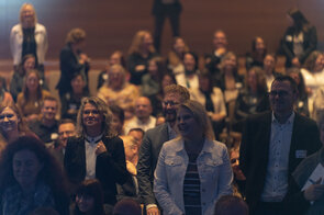 Eine Gruppe von Menschen steht in einem Raum, viele l&auml;cheln und scheinen an einer Veranstaltung teilzunehmen.