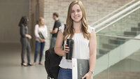 Studentin mit Kaffeebecher und Unterlagen in der Hochschule