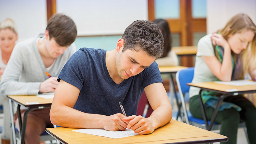 Vier Studierende sitzen an Tischen im Seminarraum und schreiben auf Papier
