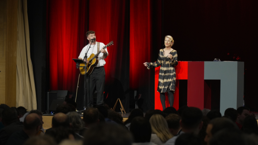 Ein Musiker mit Gitarre steht auf der Bühne, während eine Sängerin in einem gestreiften Kleid das Publikum begeistert.